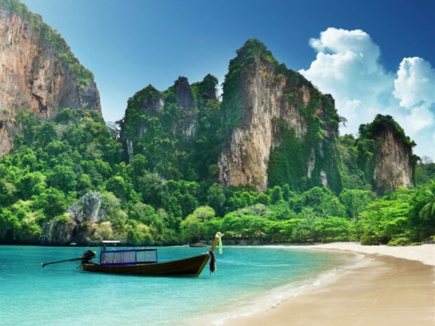 A tropical summer landscape with a boat floating near lush green cliffs and clear turquoise water