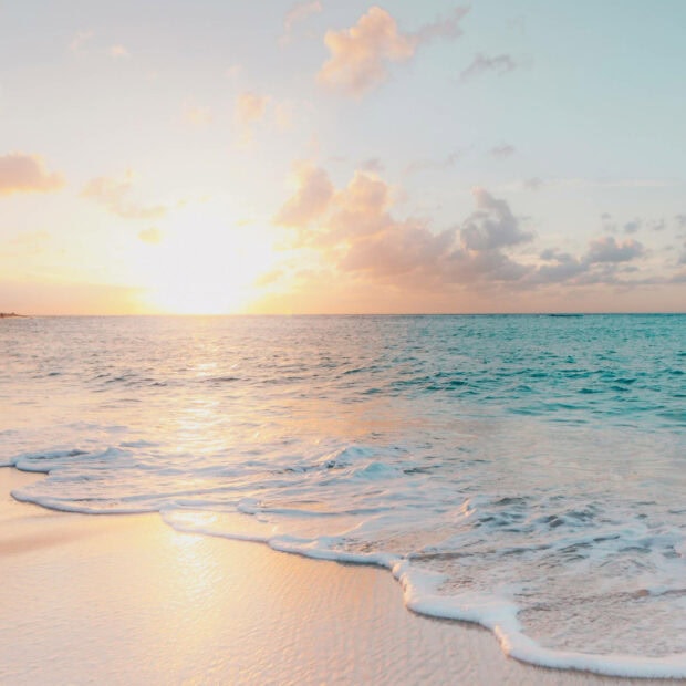 Calm ocean waves at sunset on a summer beach with soft sand and clear sky