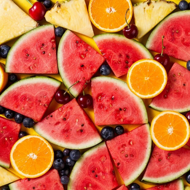 Fresh watermelon slices with cherries blueberries and orange halves on yellow background