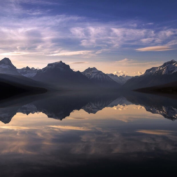 Mountain range reflection on a calm lake with summer sky clouds at sunset