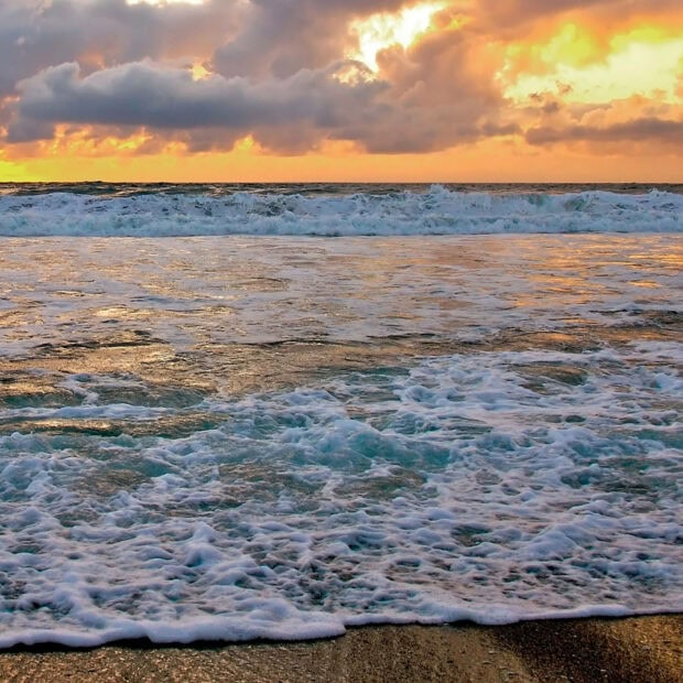Ocean waves under a summer sky at sunset with warm colors and peaceful clouds