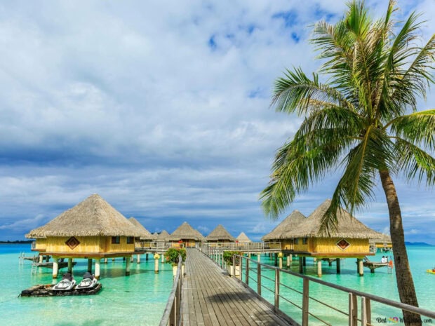 Tropical island with bungalow huts over clear water under summer sky