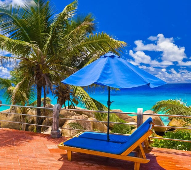 Tropical palm trees and lounge chair under blue umbrella by the ocean in summer