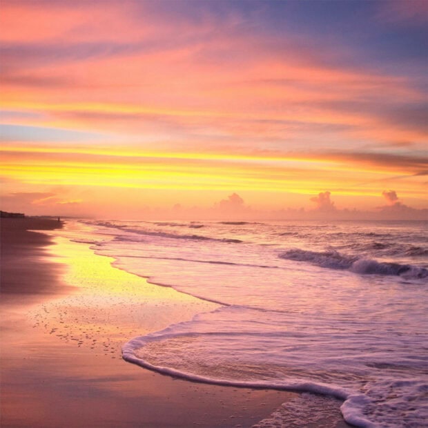 Calm summer beach with gentle waves and colorful sky at sunset