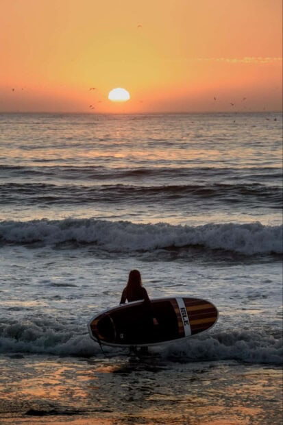 Surfer preparing to enter ocean during summer sunset
