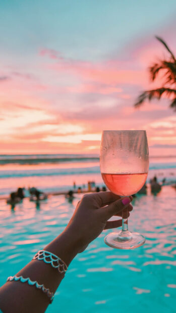 Hand holding a glass of wine near a pool during a summer sunset