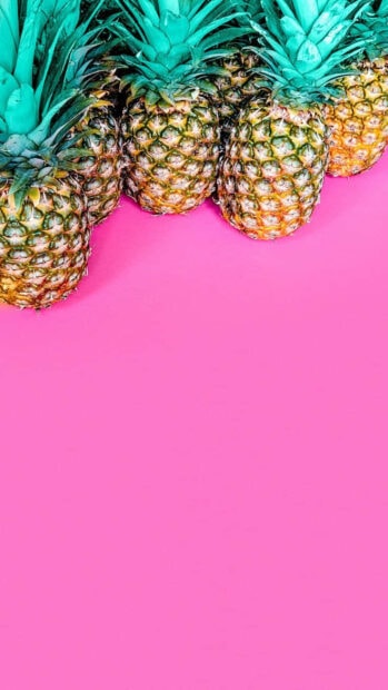 Fresh pineapples lined up on a vibrant pink surface representing summer fruit