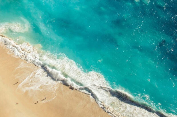 Aerial view of turquoise ocean waves crashing on sandy beach during summertime