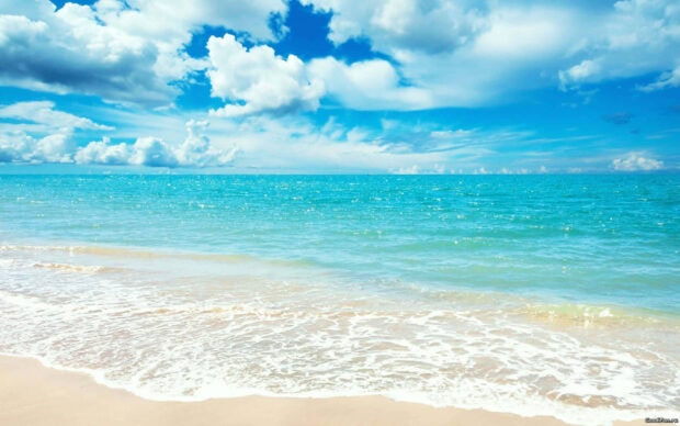 Clear blue ocean waves on a sandy beach under a bright sky with clouds
