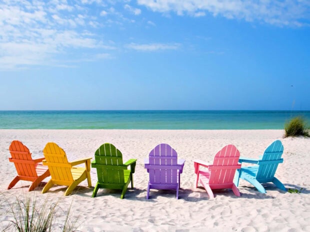 Colorful beach chairs lined up on white sand under a clear blue sky at the seaside