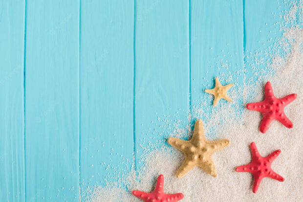 Starfish and sand on a blue wooden surface with summertime vibes