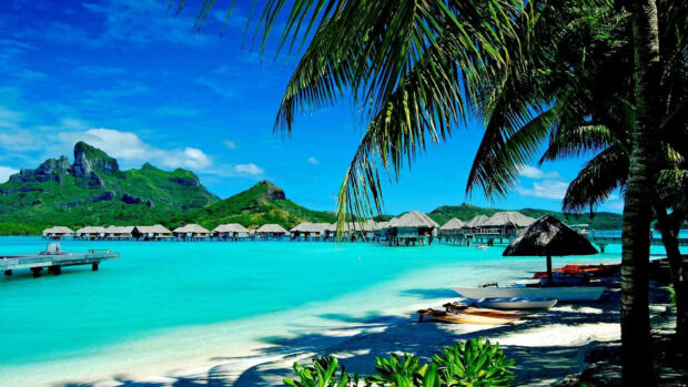 Turquoise ocean and tropical island with palm trees and huts during summertime