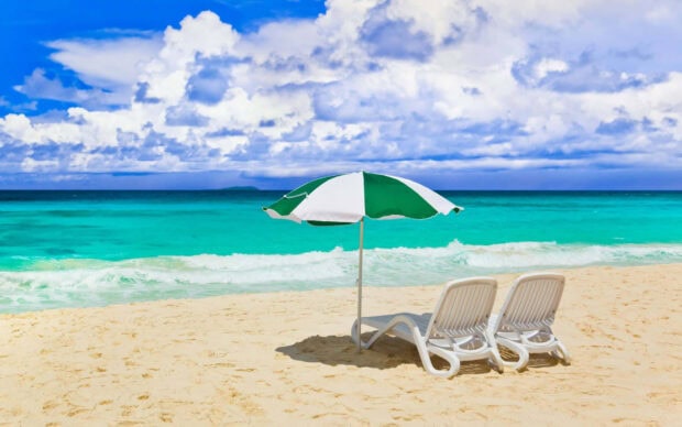 Two beach chairs under a green and white umbrella on turquoise ocean shore