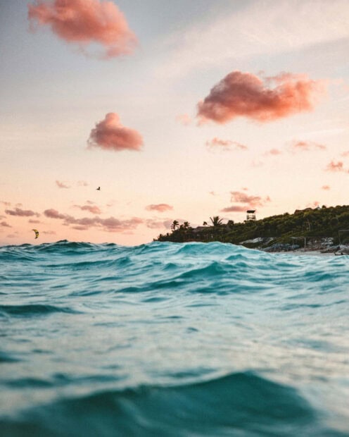 Calm ocean waves with tropical coastline under a pastel sunset sky