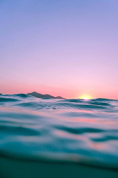 Ocean waves with sunset and mountain silhouette in summertime scene