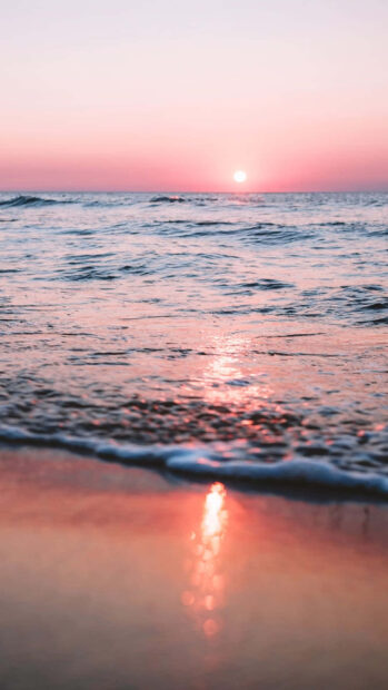 Pink sunset over calm ocean waves reflecting on the shore during summertime