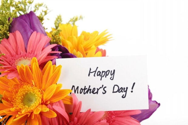 A vibrant bouquet of pink, orange, and yellow gerbera daisies displays a white card reading 