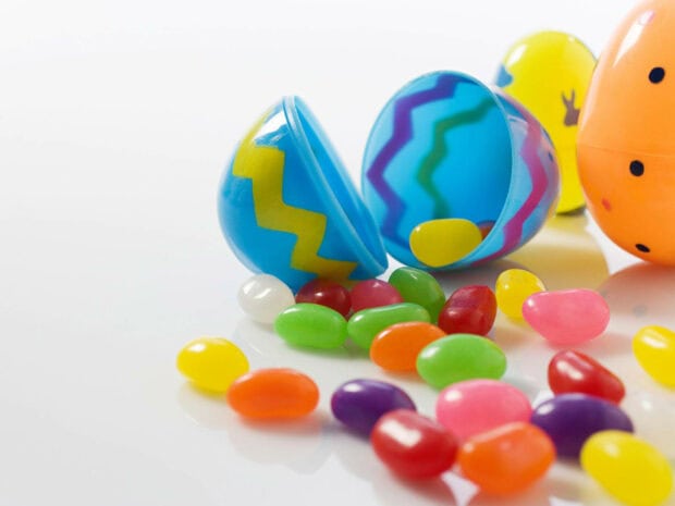 Assorted jelly beans spill from open plastic eggs, bright colors scatter on a white surface, ready for a playful hunt