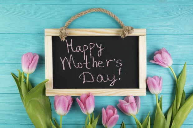 Pink tulips frame a small blackboard displaying a chalk message on a light blue wooden surface