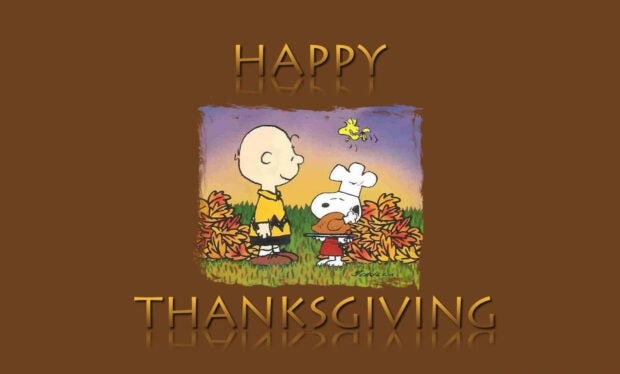 Charlie Brown and Snoopy stand among colorful autumn leaves, with Snoopy wearing a chef's hat and presenting a small turkey