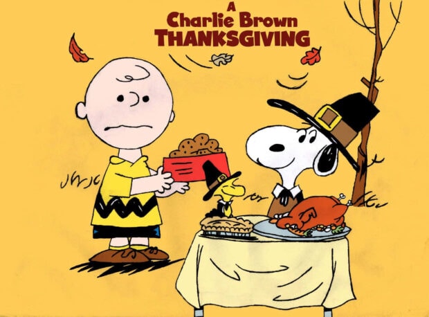 Charlie Brown, Snoopy, and Woodstock gather around a small table laden with popcorn, pie, and a roasted turkey, all dressed in pilgrim attire