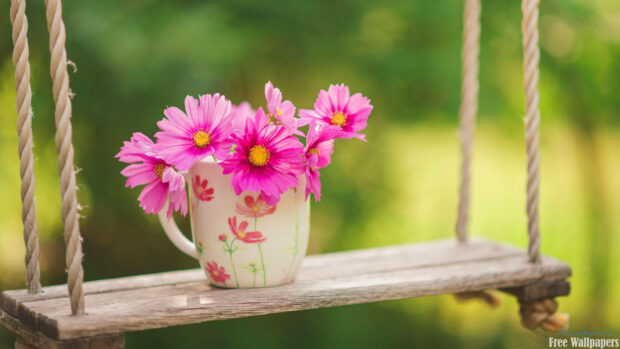 Pink cosmos fill a patterned mug resting on a rustic wooden swing in a verdant garden