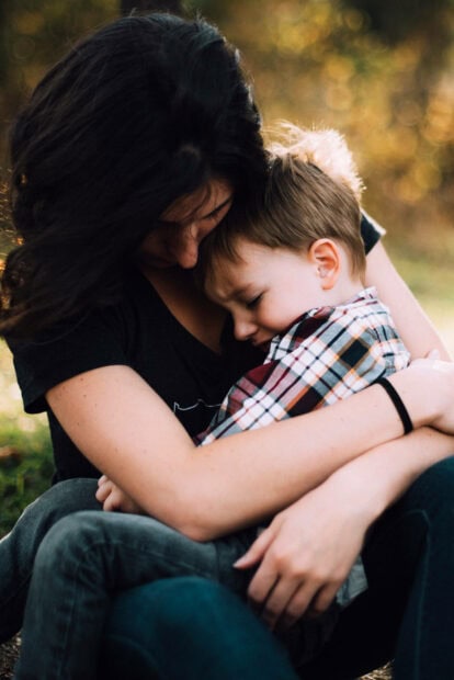 Woman embraces young child, comforting them outdoors with soft light