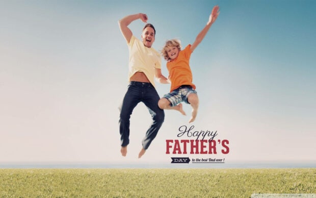 A father and his young son jump high, laughing, with arms spread against a clear blue sky above a green field