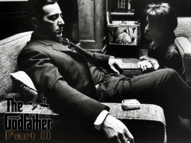Michael Corleone (Al Pacino) reclines on a sofa, holding hands with his son in a poignant black and white scene from the film, displaying the 