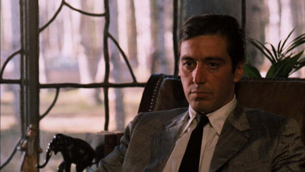 A young man sits thoughtfully in an armchair beside a large window, dressed in a sharp suit