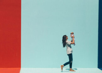 A woman lifts her smiling baby against a vibrant backdrop of colored walls, celebrating their bond