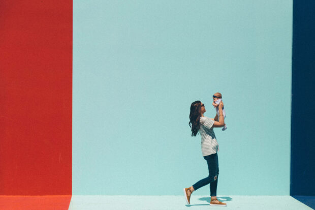 A woman lifts her smiling baby against a vibrant backdrop of colored walls, celebrating their bond