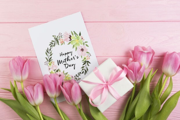 Pink tulips arrange on a wooden surface, a floral greeting card rests beside a small gift box