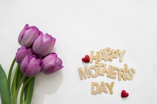A bouquet of purple tulips arranges beside wooden letters spelling 