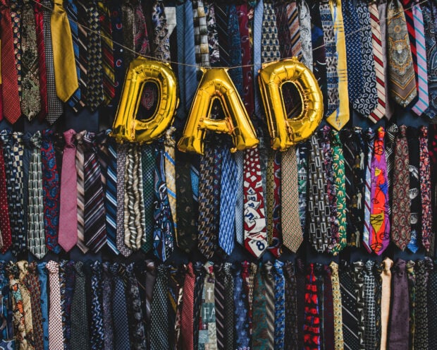 Many colorful neckties hang vertically as golden balloons spell DAD across a vibrant display