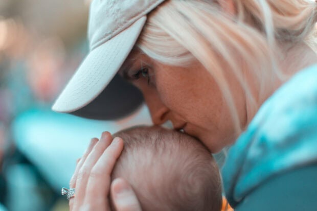 Woman gently kisses baby's forehead, cradling the infant's head with her hand