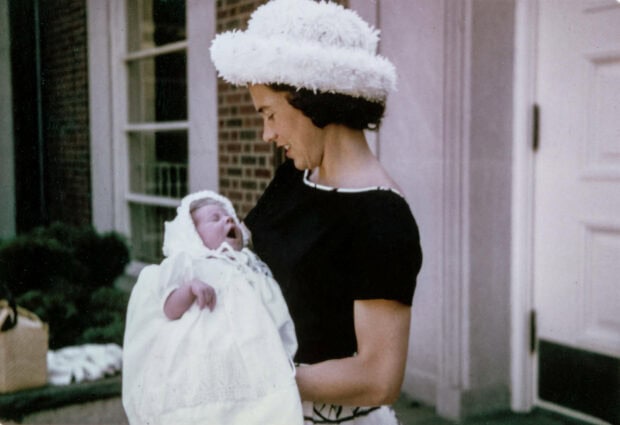 Woman cradles infant swaddled in white, smiling gently outdoors