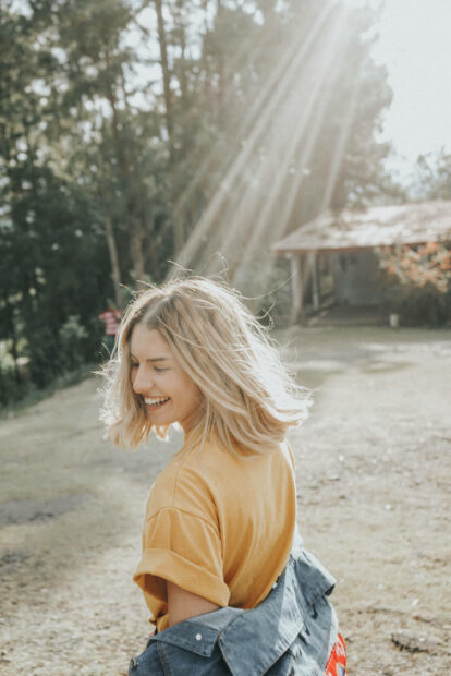 A young woman smiles, turning her head as sun rays stream through her blonde hair in a vibrant outdoor setting