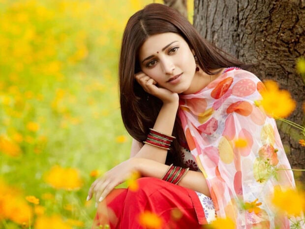 A woman sits gracefully by a tree trunk, surrounded by a vibrant field of yellow blooms while gazing forward