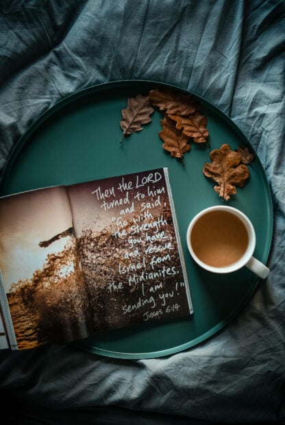 Aesthetic fall wallpaper displaying an open book, a warm cup of coffee, and brown autumn leaves on a teal tray on a dark gray bed