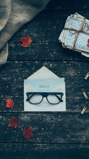 Aesthetic Fall Wallpaper featuring a dark wooden table with an open envelope, black glasses, and scattered red autumn leaves
