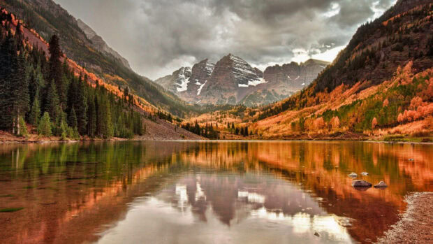 An aesthetic fall wallpaper featuring the stunning Maroon Bells mountains reflecting in a clear lake surrounded by colorful autumn trees