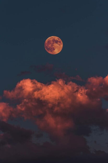 Aesthetic Fall Wallpaper featuring a full orange moon glowing above warm reddish-orange clouds in a dark blue sky
