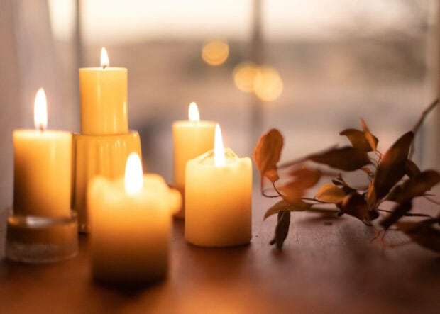 An aesthetic fall wallpaper featuring a warm, inviting scene of several lit pillar candles and a branch with autumn leaves, casting a soft glow