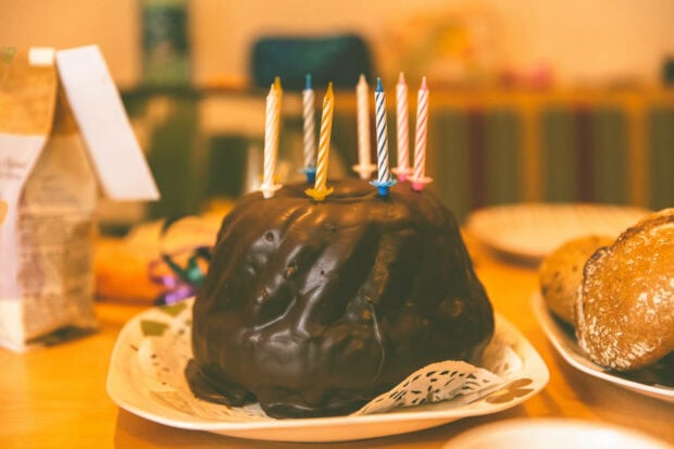 A delicious birthday wallpaper featuring a dark chocolate bundt cake topped with lit colorful candles on a table