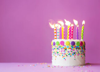 A vibrant birthday wallpaper featuring a white cake with colorful sprinkles and lit candles against a simple purple background