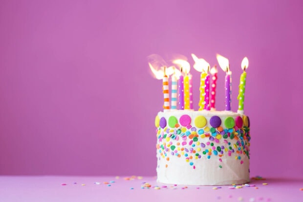 A vibrant birthday wallpaper featuring a white cake with colorful sprinkles and lit candles against a simple purple background