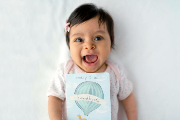 A cute birthday wallpaper showing a happy baby holding a '3 months old' milestone card
