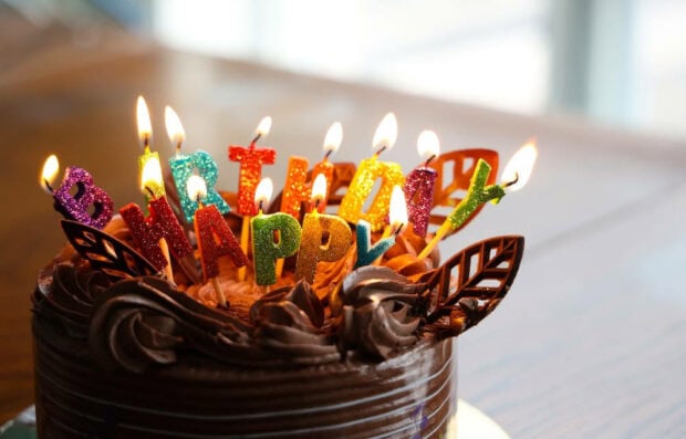 A heartwarming birthday wallpaper featuring a chocolate cake topped with glowing 'Happy Birthday' letter candles