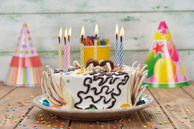 A cheerful birthday wallpaper showcasing a white cake with lit candles, surrounded by colorful confetti and party hats on a wooden table